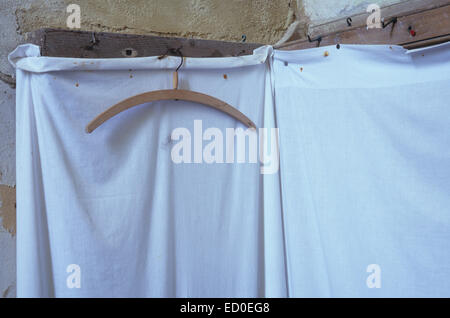 Wooden coat-hanger hanging from row of old coat-hooks with sheet attached to protect clothes from flaking wall Stock Photo