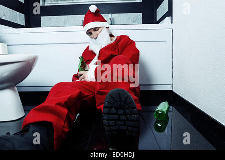 drunken santa claus sleeping at bathroom with beer bottle in hand Stock Photo