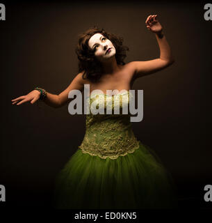 Fantasy makeover photography: A young woman girl model made up to look like a porcelain white-faced painted puppet and posing like a real-life doll in a photo studio wearing a big green frock dress ball gown Stock Photo