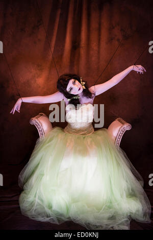 Fantasy makeover photography: A young woman girl model made up to look like a porcelain white-faced painted puppet and posing like a doll in a photo studio wearing a big green frock dress ball gown Stock Photo