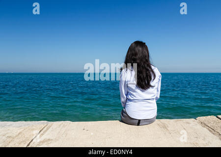 Young Asian woman sits at Lake Michigan in the Hyde Park area of Chicago, IL, USA on a sunny day. Stock Photo
