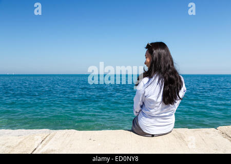 Young Asian woman sits at Lake Michigan in the Hyde Park area of Chicago, IL, USA on a sunny day. Stock Photo