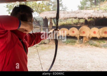 Person shooting arrows from a bow, practicing archery in Zhanhjiajie, China Stock Photo