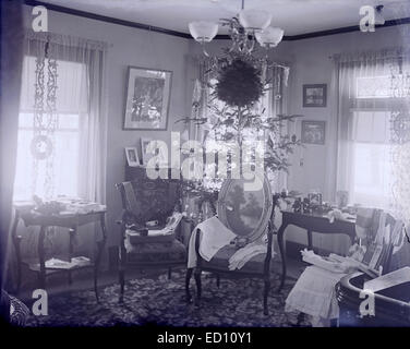Antique, circa 1906 image, Christmas tree with opened presents on display, Boston, Massachusetts, USA. The book "Jane Cable" by George Barr McCutcheon, the fifth best-selling novel in the United States in 1906, is visible on the chair. Stock Photo