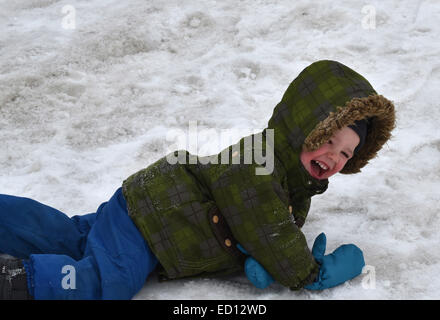 A young boy (2 1/2 yrs) laughing rolling in the snow Stock Photo