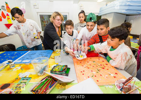 A graphic designer, 2nd from left, works with refugee children in a refugee accomodation. Stock Photo