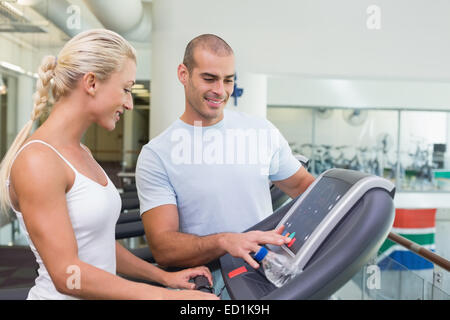 Trainer assisting woman with treadmill screen options at gym Stock Photo