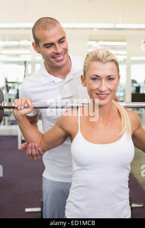 Trainer helping woman with lifting barbell in gym Stock Photo