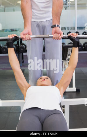 Trainer helping woman with lifting barbell in gym Stock Photo