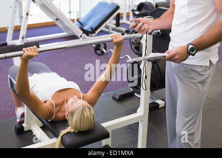 Trainer with clipboard besides woman lifting barbell in gym