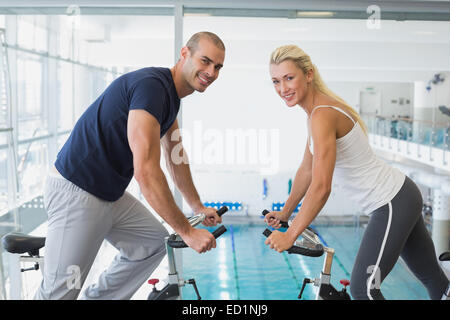 Side view of smiling couple working on exercise bikes at gym Stock Photo