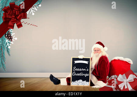 Composite image of santa sits leaned on his bag with a board Stock Photo