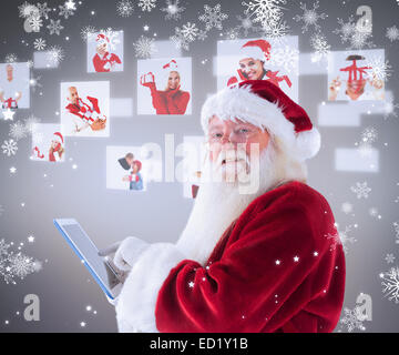 Composite image of santa uses a tablet pc and smiles into the camera Stock Photo