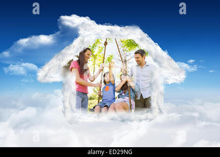 Composite image of happy couple pushing kids on swing Stock Photo