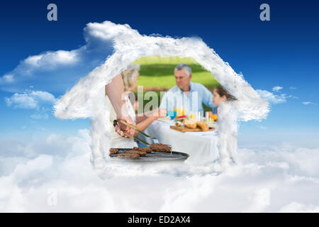 Composite image of barbecue grill with extended family having lunch in park Stock Photo