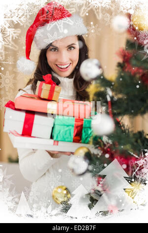 Composite image of festive brunette holding pile of gifts near a christmas tree Stock Photo