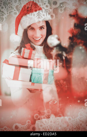 Composite image of festive brunette holding pile of gifts near a christmas tree Stock Photo