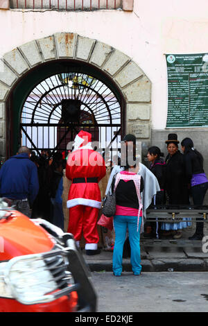 La Paz, Bolivia, 24th December 2014. Father Christmas waits with other visitors outside the infamous San Pedro prison. All visitors have to have their bags searched before entering to visit family members inside the jail. Many children accompany their convicted parents inside prisons in Bolivia as there is often nowhere else for them to live; social organisations often take presents to the country's prisons for them at Christmas time. Credit:  James Brunker / Alamy Live News Stock Photo
