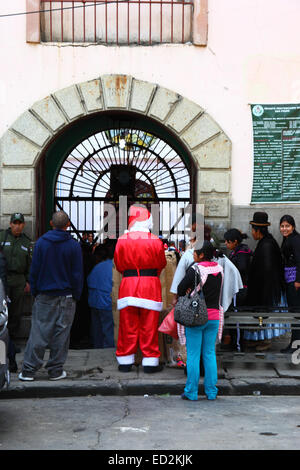 La Paz, Bolivia, 24th December 2014. Father Christmas waits with other visitors outside the infamous San Pedro prison. All visitors have to have their bags searched before entering to visit family members inside the jail. Many children accompany their convicted parents inside prisons in Bolivia as there is often nowhere else for them to live; social organisations often take presents to the country's prisons for them at Christmas time. Credit:  James Brunker / Alamy Live News Stock Photo