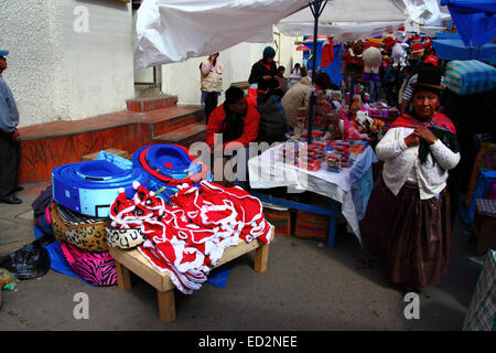 La Paz, Bolivia, 24th December 2014. An Aymara woman or cholita wearing traditional dress walks past a stall selling Santa Claus dog coats in a Christmas market. Credit:  James Brunker / Alamy Live News Stock Photo