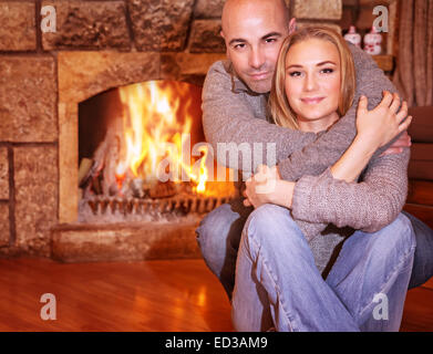 Portrait of gentle couple sitting near fireplace at home, romantic celebration of Christmas holidays, love and togetherness Stock Photo