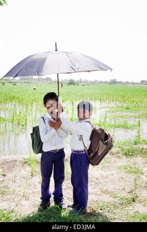 2 indian rural children boys students holding Umbrella rain season enjoy Stock Photo