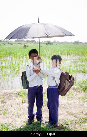 2 indian rural children boys students holding Umbrella rain season enjoy Stock Photo