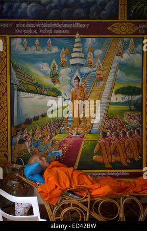 CHIANG MAI, THAILAND - NOVEMBER 5, 2014: Buddhist monk lies resting under religious artwork at the entrance to a temple. Stock Photo