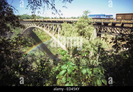 Train crossing the bridge over the Zambezi river on the Zimbabwe/ Zambia border with a rainbow, Victoria Falls, Zimbabwe Stock Photo