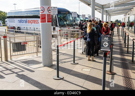 Travelers wait in a queue before boarding National Express bus at London Stansted Airport Essex England United Kingdom UK Stock Photo