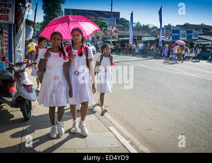 Schoolgirls in white uniforms and pink polka dot umbrella and election posters of ruling president Mahinda Rajapaksa, Sri Lanka. Stock Photo