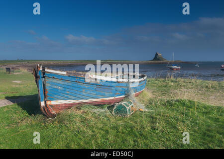 Lindisfarne Castle viewed from across the bay on Holy Island. There is a boat and a lobster pot on the beach in front of Holy Island Harbour. Stock Photo