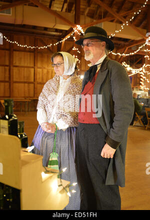 Old Bethpage, New York, USA. 26th Dec, 2014. SHERRI GUTHRIE and husband CHART GUTHRIE, dressed in traditional 19th Century clothing, visit the Salce imported Italian olive oil booth inside the Barn, at night, on the historic grounds of Old Bethpage Village Restoration, transformed by candlelight and Christmas decorations into a Nineteenth Century holiday experience for Long Island visitors. © Ann Parry/ZUMA Wire/Alamy Live News Stock Photo