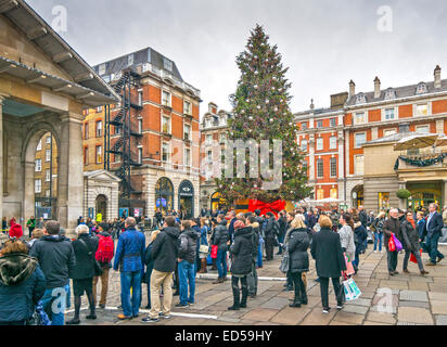 LONDON A CHRISTMAS TREE IN COVENT GARDEN WITH SPECTATORS WATCHING ACROBATS Stock Photo