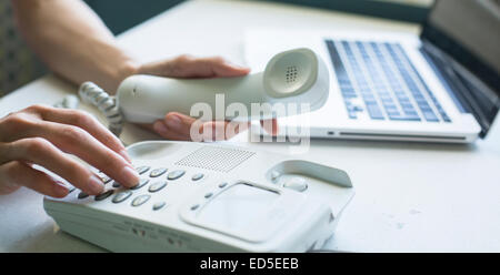 Female hands using phone, laptop at background. Stock Photo