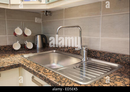 Kitchen sink with tap on marble counter and kettle next to mug tree in apartment Stock Photo