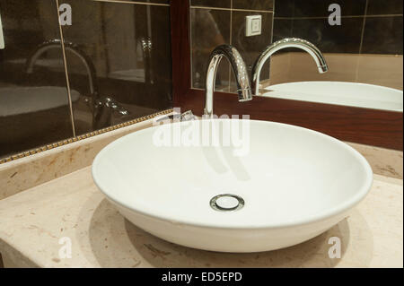 Ornate white sink on marble counter next to mirror in luxury apartment bathroom Stock Photo