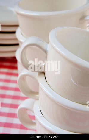 a pile of empty porcelain coffee cups and plates on a checkered tablecloth Stock Photo