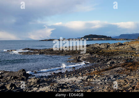 View of incoming tide and breakers on the rocky foreshore looking towards Ellenabeich on a brisk winter day in Scotland Stock Photo