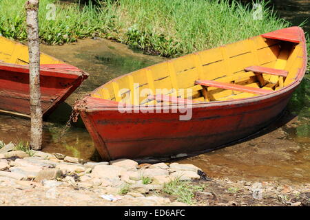 Red-orange and yellow colored wooden rowboats chained to a stake at the foot of Ananda hill on the shore of the Phewa tal-lake. Stock Photo