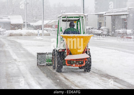 Small snowplow removing snow from sidewalk and sprinkled salt antifreeze Stock Photo