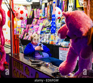 A bored young man teenage boy checking his mobile phone while working on a stall at Aberystwyth november fair, Wales UK Stock Photo