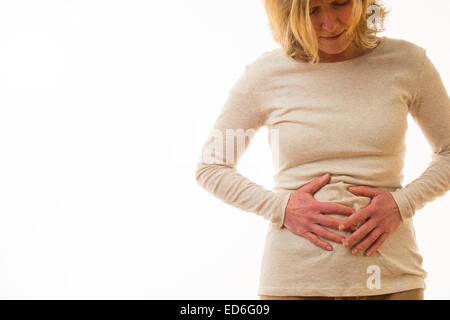 A forty year old caucasian woman with belly ache period pre menstrual tension pains rubbing her painful stomach, standing against a white background. UK Stock Photo