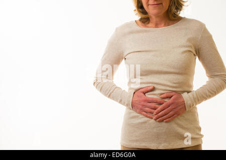 A forty year old caucasian woman with belly ache period pre menstrual tension pains rubbing her painful stomach, standing against a white background. UK Stock Photo