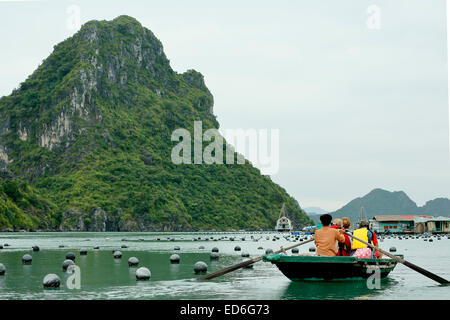 Tourists on wooden row boats, pearl farm buoys and limestone (karst) mounds, Vung Vieng fishing village, Ha Long Bay, Vietnam Stock Photo