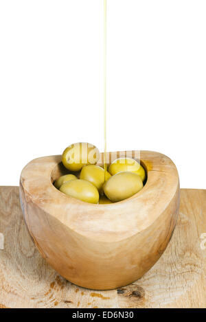 olive oil in thin trickle flows on olives in wooden bowl close up isolated on white background Stock Photo