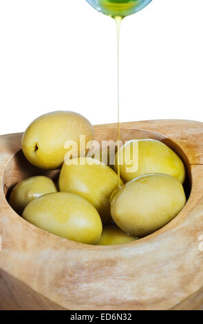 olive oil in thin stream flows from bottle on green olives in wooden bowl close up isolated on white background Stock Photo