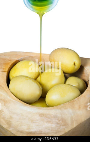 olive oil in thin trickle flows from bottle on green olives in wooden bowl close up isolated on white background Stock Photo