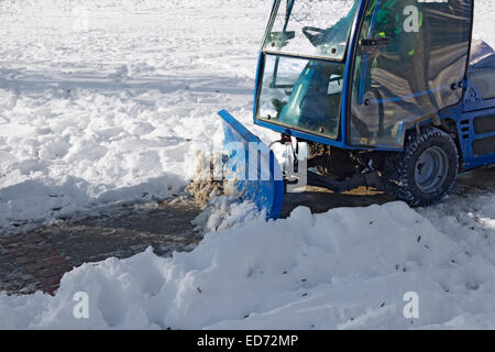 Blue snowplow removing snow from sidewalk and sprinkled salt antifreeze Stock Photo