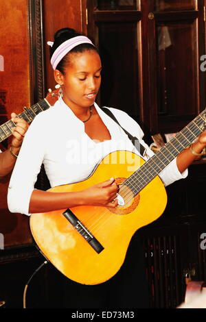 African Cuban Young adult musician guitarist woman playing (performing) classical acoustic guitar in a band. Havana, Cuba Stock Photo